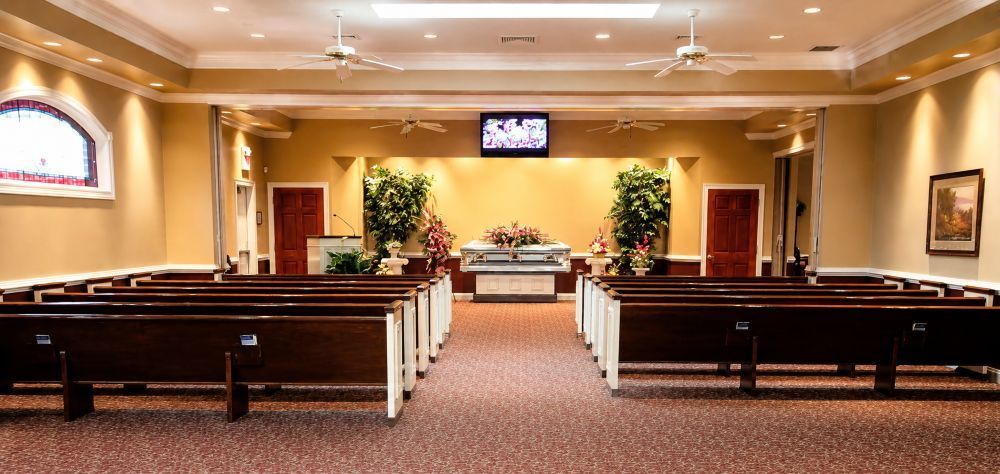 Funeral Homes in York, PA chapel interior with wooden pews, floral tributes, and casket display