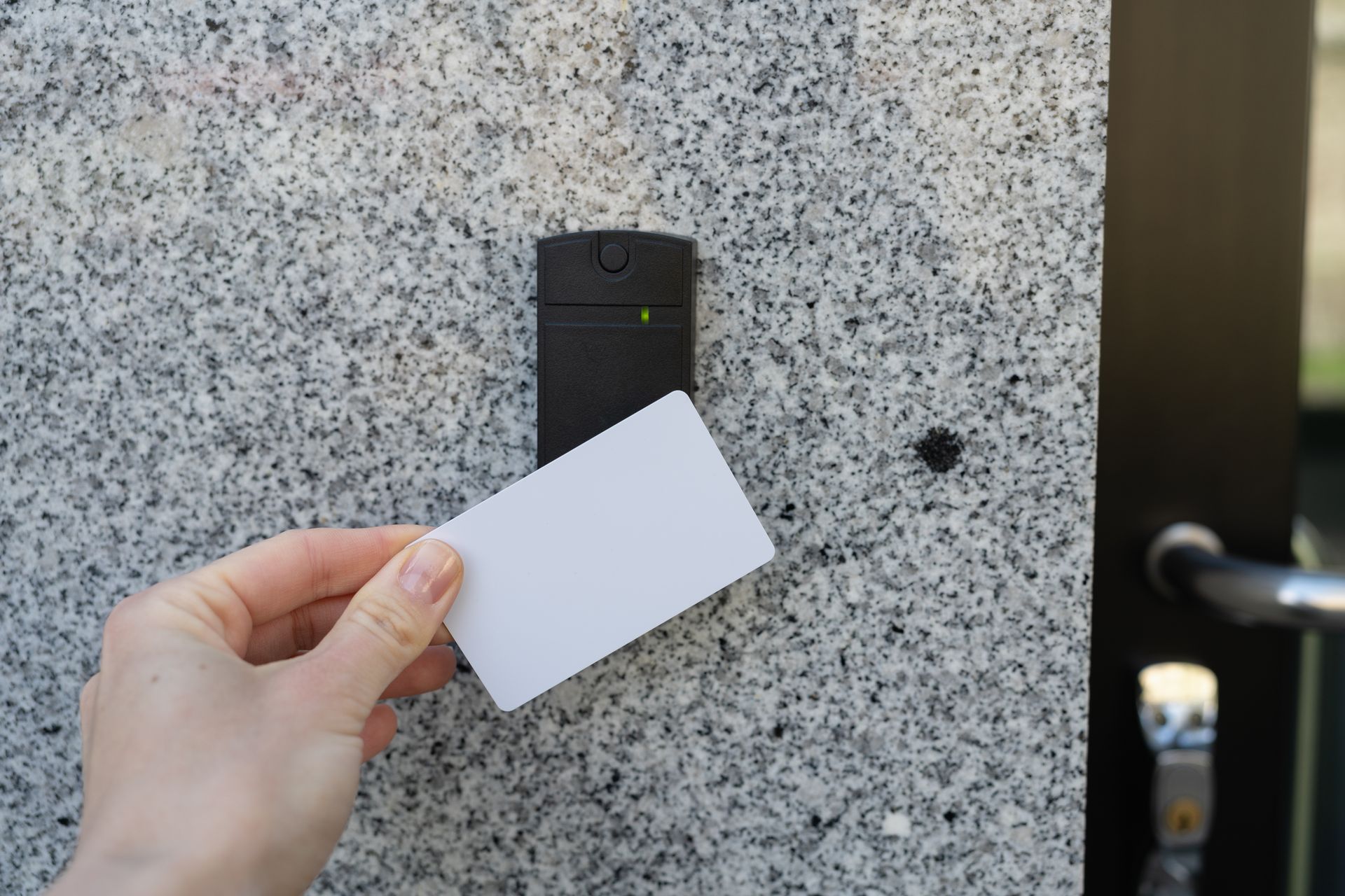 Hand holding a keycard to a card reader beside a commercial glass door