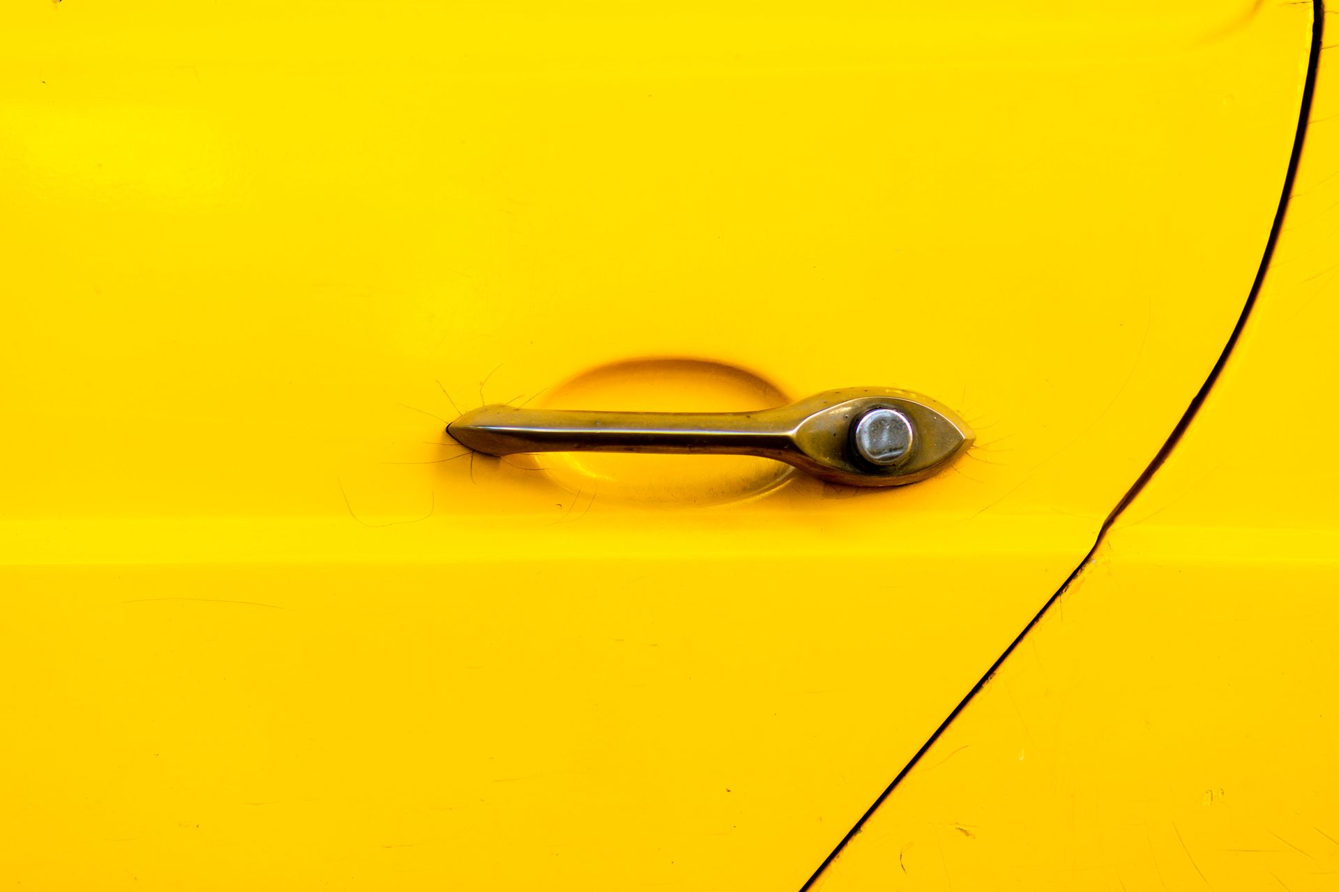 Close-up of a vintage yellow car door with a chrome handle, highlighting classic automotive.