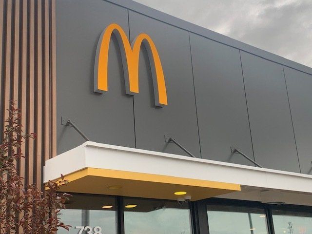 McDonald's restaurant exterior with golden arches logo. Gray building with yellow awning and door.