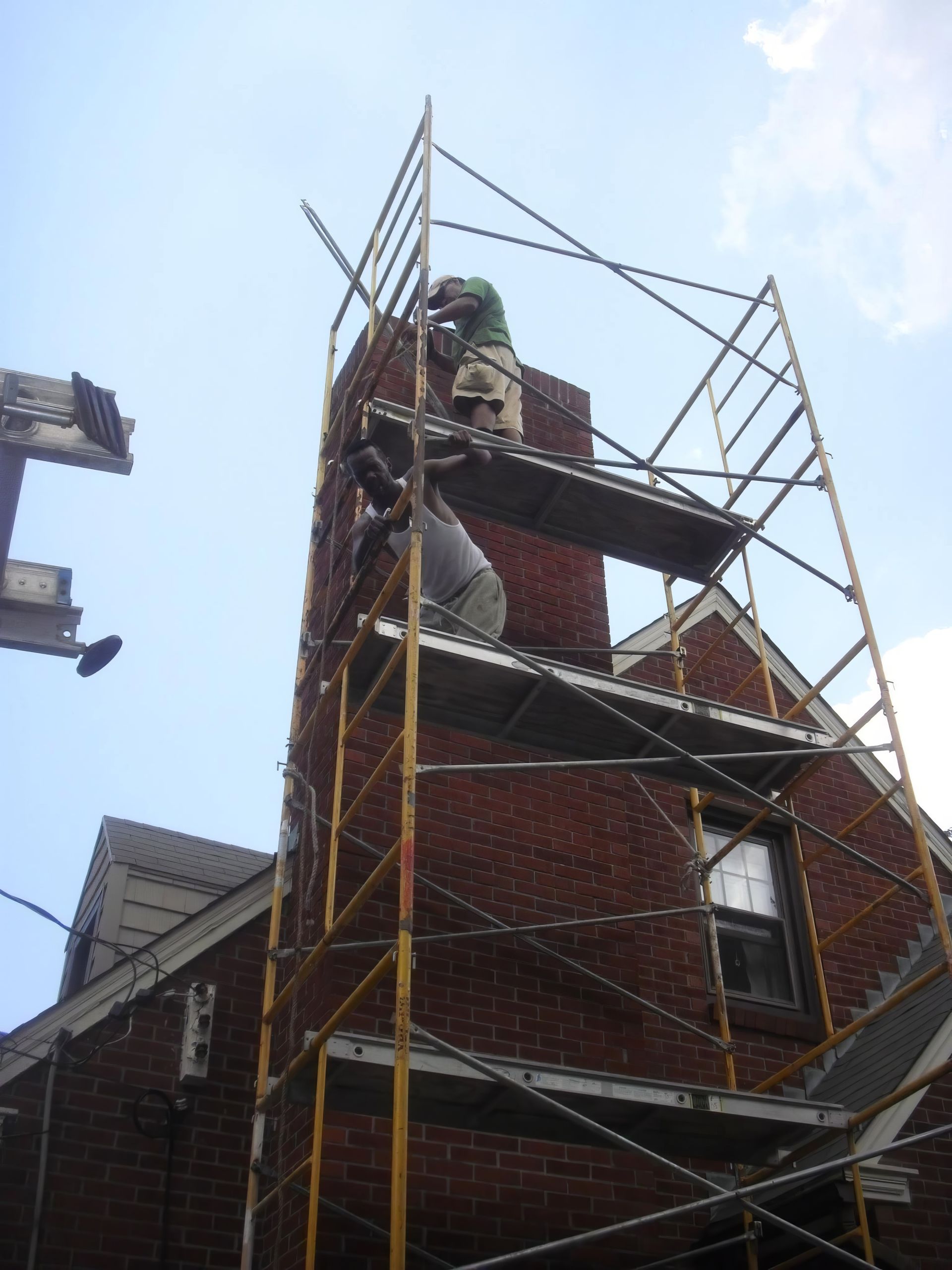 Brick building under construction with metal scaffolding and workers on top against a blue sky