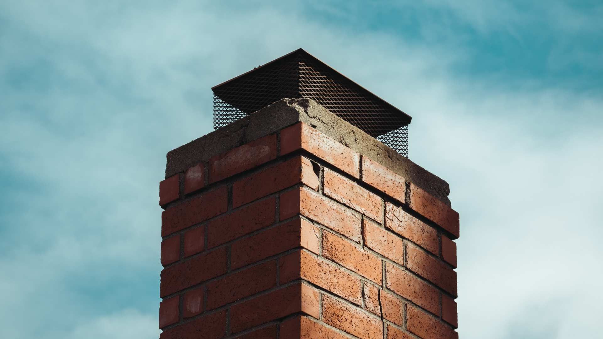 Brick chimney with a metal cap against a cloudy blue sky
