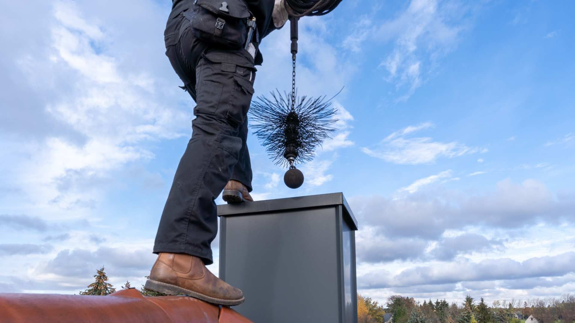 Person on a roof cleaning a chimney with a brush under a cloudy sky