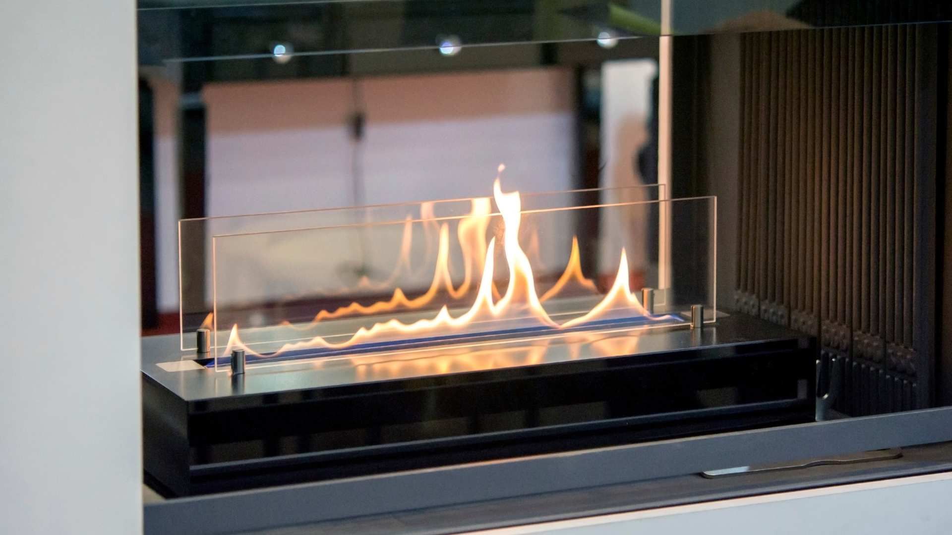 Modern glass fireplace with tall orange flames in a sleek indoor setting