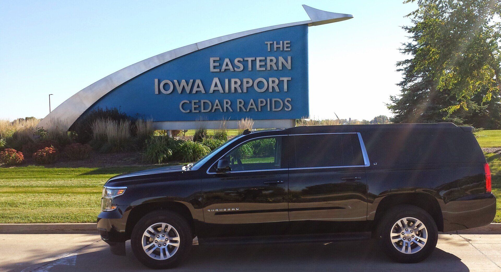 A black Chevrolet Suburban, serving as a Cedar Rapids Airport Transportation vehicle, is parked in front of a large sign that reads