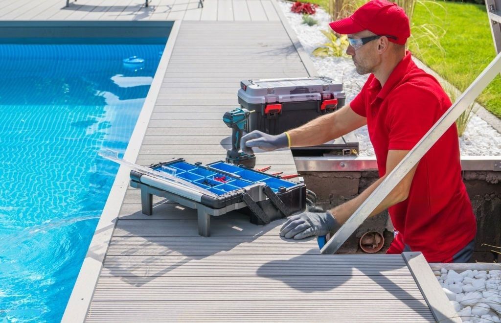 A man is working on a deck next to a swimming pool.