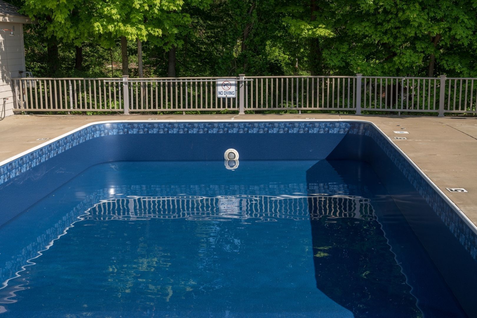 An empty swimming pool with a fence around it and trees in the background.