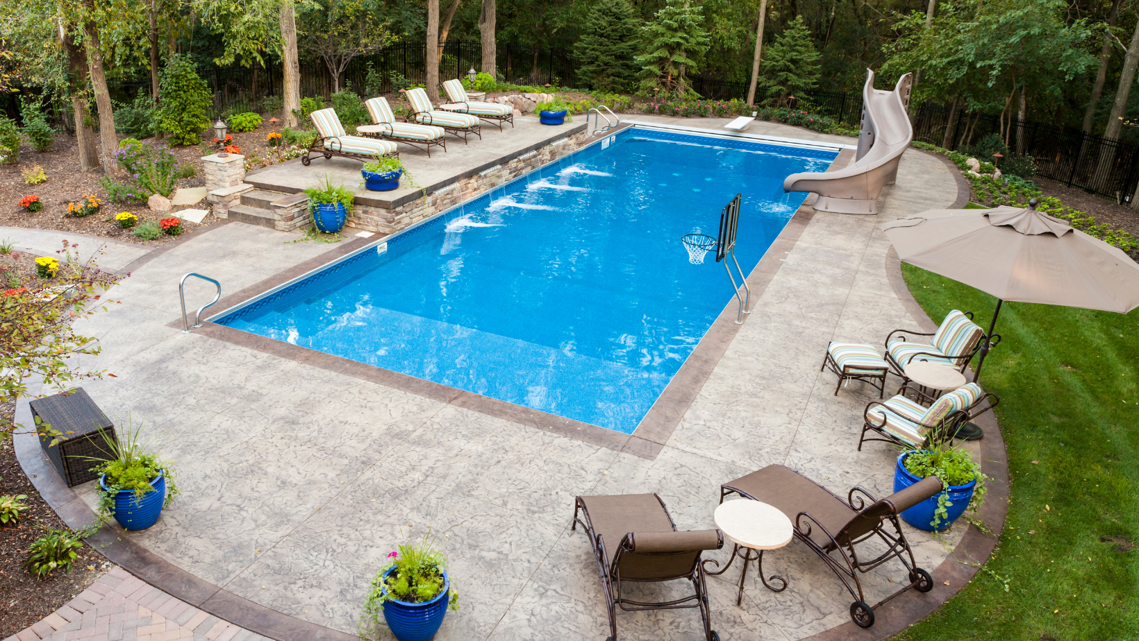 A large swimming pool with a slide in the backyard surrounded by chairs and umbrellas.