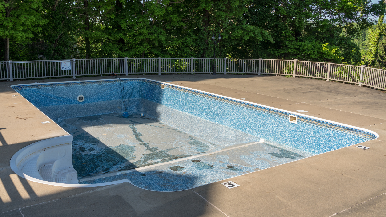 An empty swimming pool with a fence around it and trees in the background.