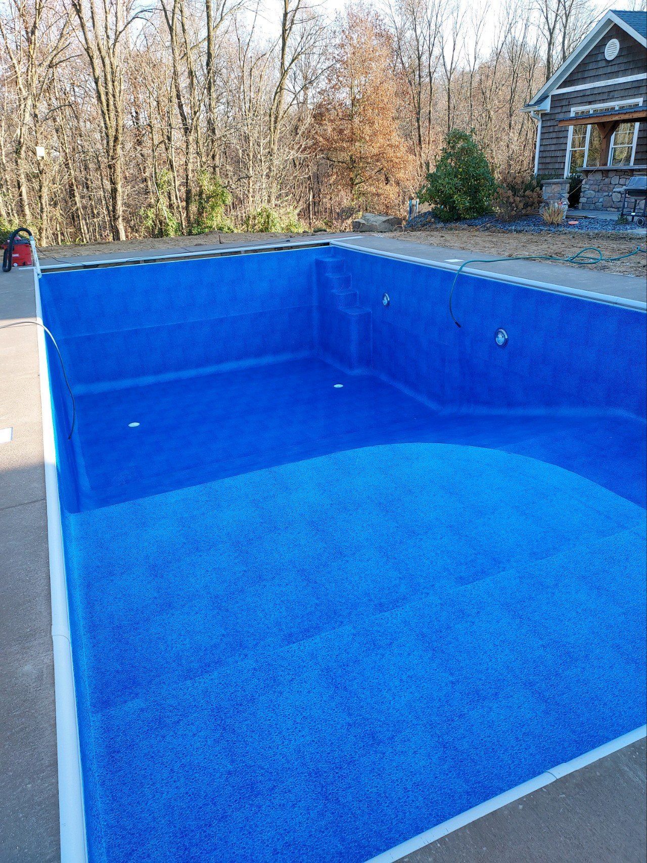 A large blue swimming pool is sitting in front of a house.