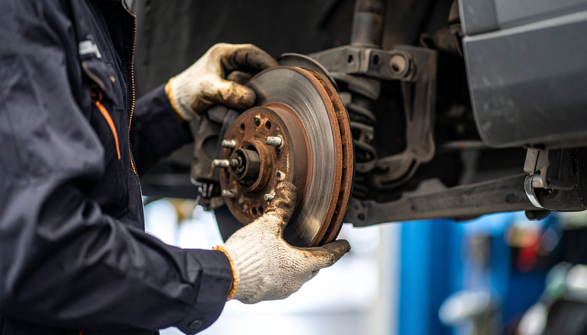Mechanic in gloves removing a worn brake rotor from a vehicle lifted in an auto repair shop