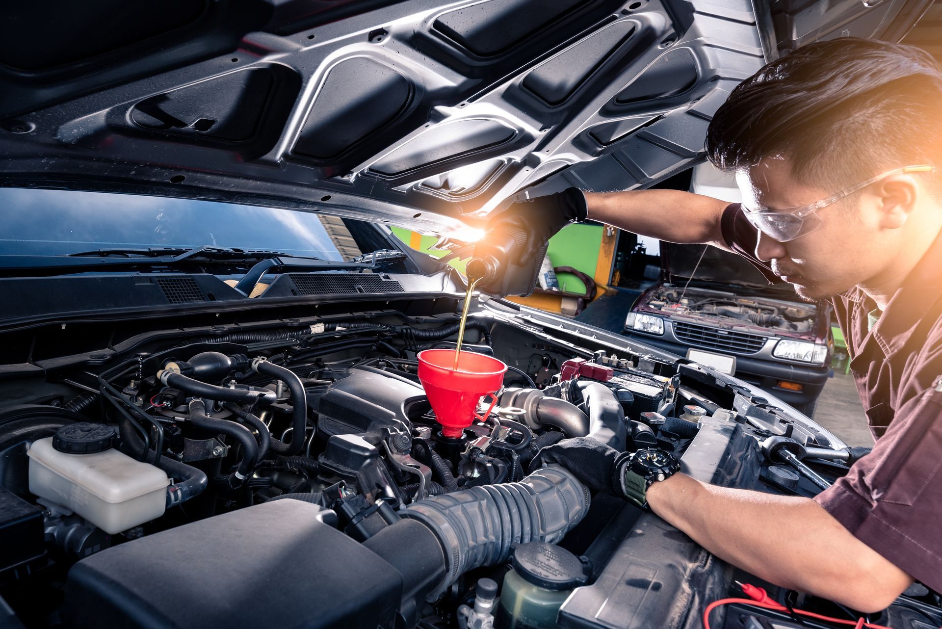 Auto mechanic pouring oil into a vehicle engine during an oil change service in a repair shop
