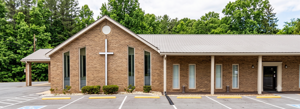 Brick church building with white cross accents, arched windows, and a parking lot in front