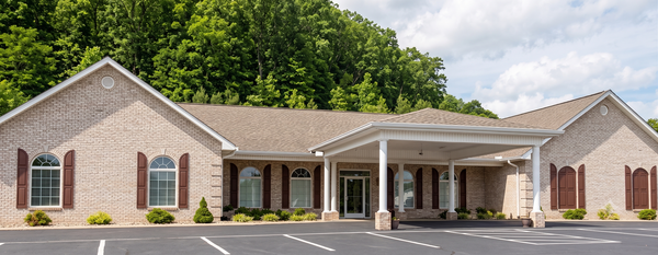 Single-story stone building with a covered entrance, brick accents, and a parking lot in front.