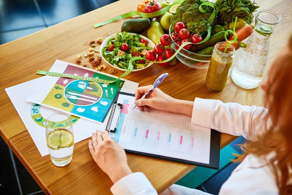 A Person Writes on a Meal Plan Chart at a Table — Cathie Barnes Holistic Wellness in Yeppoon, QLD
