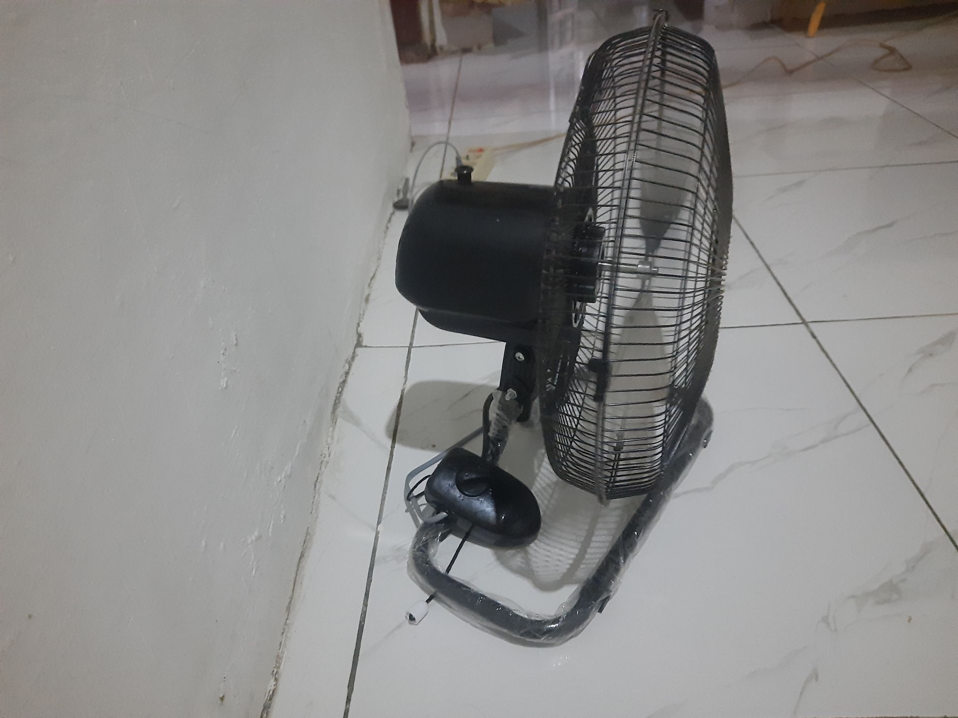 A black fan is sitting on a tiled floor next to a wall.