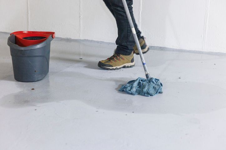 A person is mopping the floor next to a bucket.