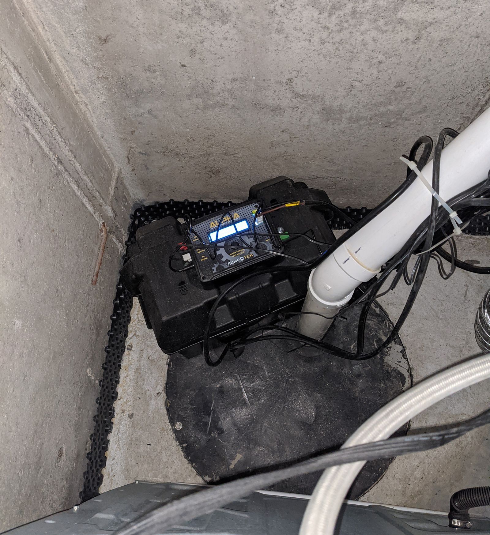 a sump pumpx is sitting on the floor next to a white pipe 