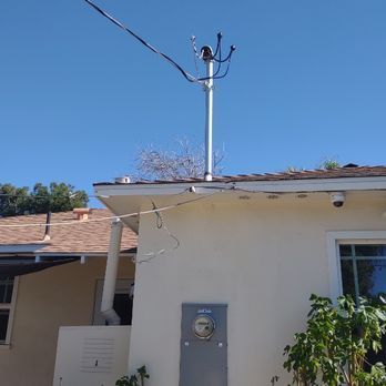Utility pole atop a house with power lines against a blue sky. A meter box is visible on the wall.