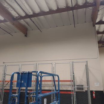Blue lift in front of a tall, light-colored wall with a chain-link fence and ceiling beams.
