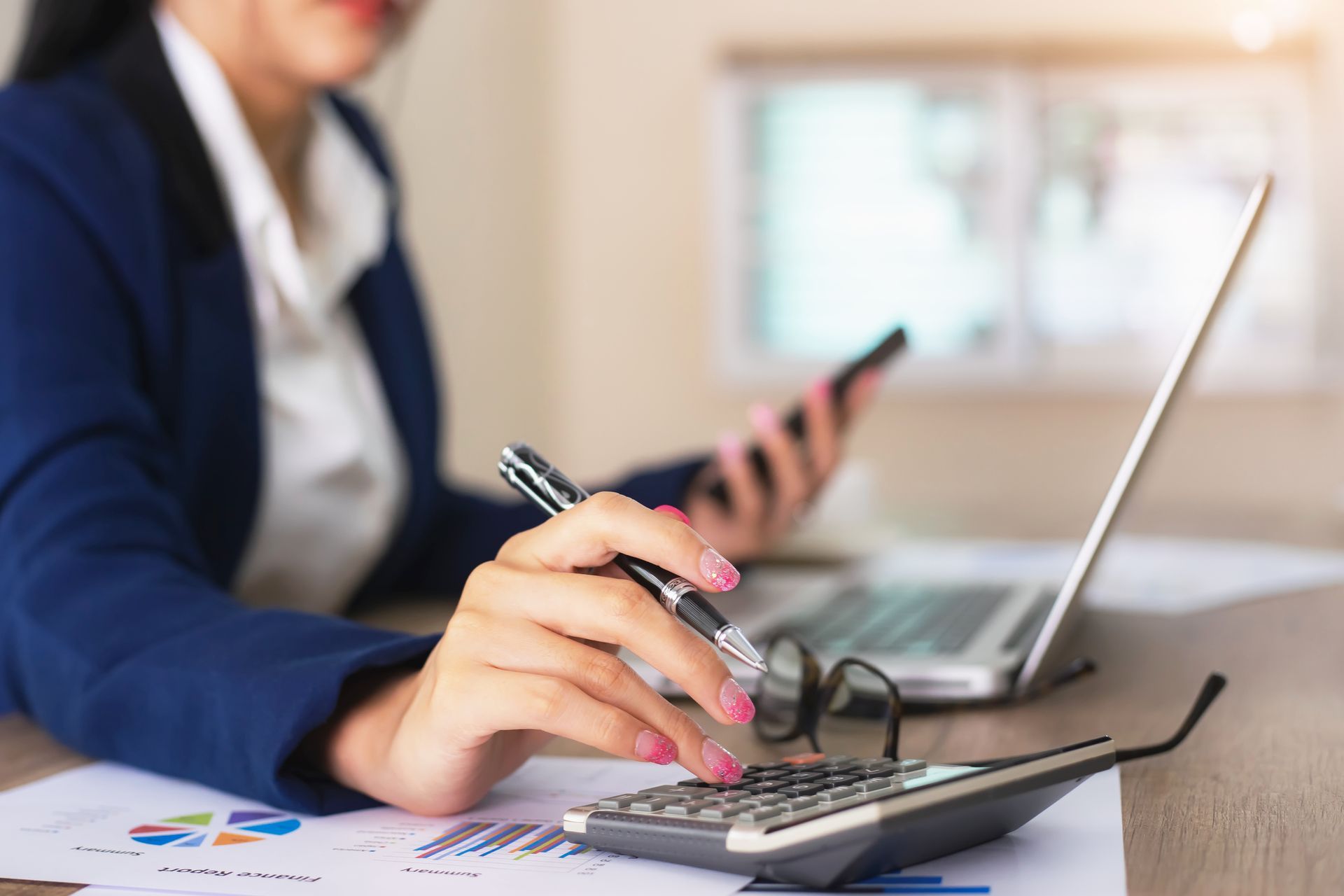 A woman is sitting at a desk using a calculator and a pen.