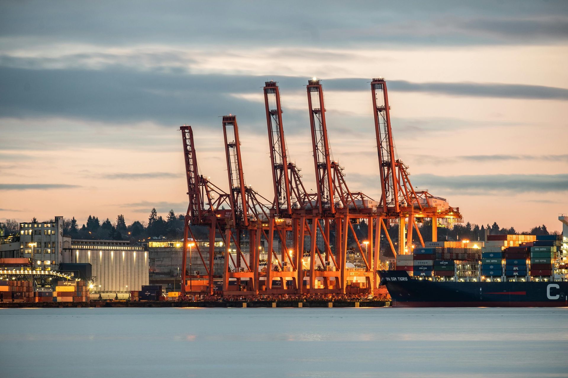 A large container ship is docked in a harbor at sunset.