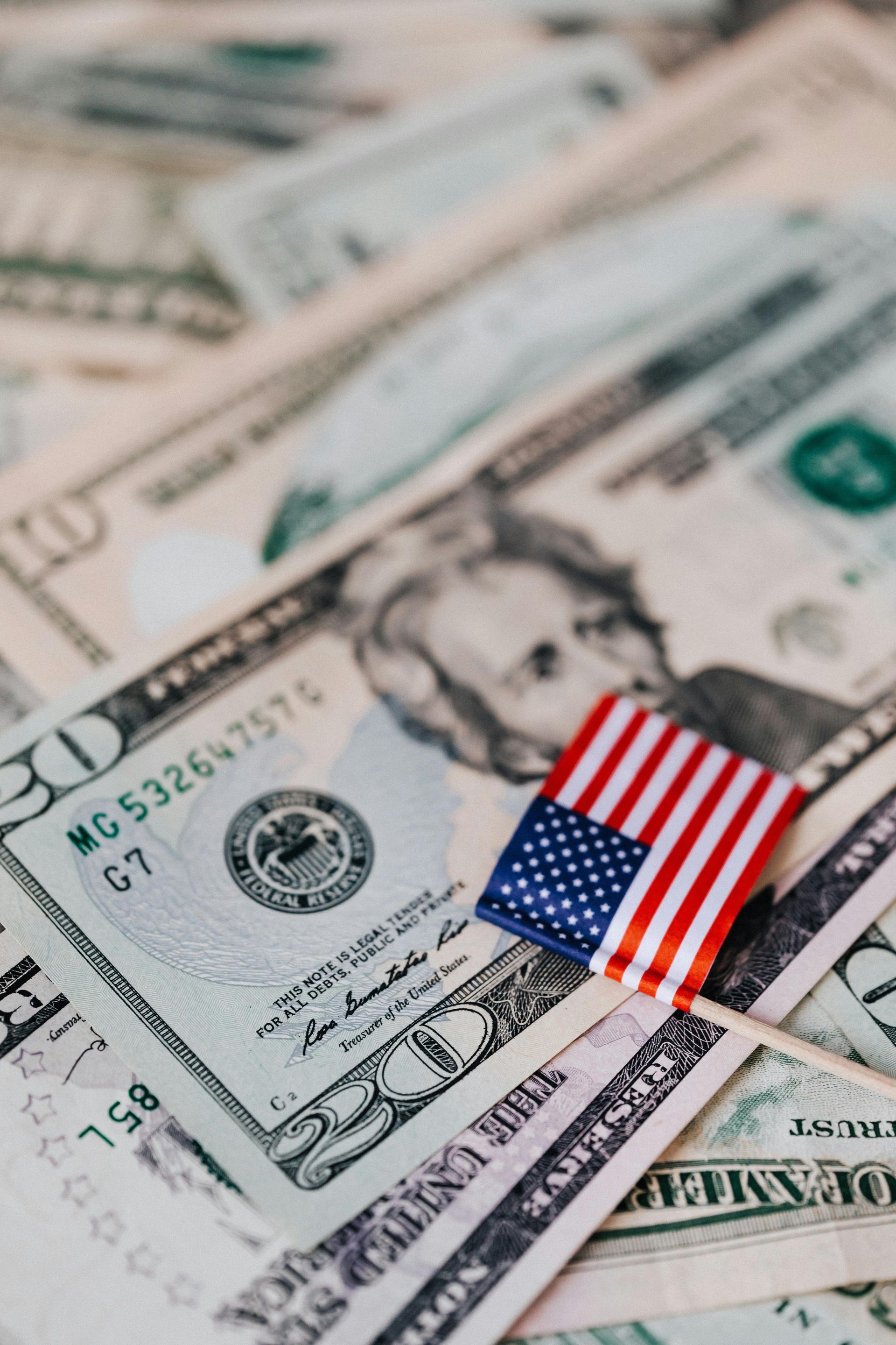 A small american flag is sitting on top of a pile of money.