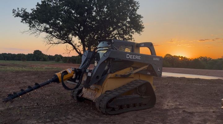Tracked excavator with auger attachment at sunset on a dirt field