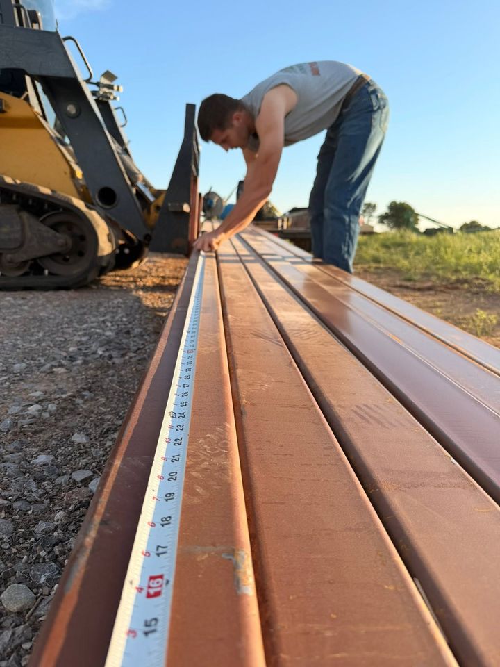 Worker measuring long copper panels on a construction site beside heavy equipment