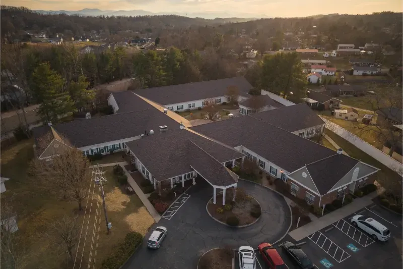 Aerial view of a large brick building with a circular driveway and parked cars at dusk