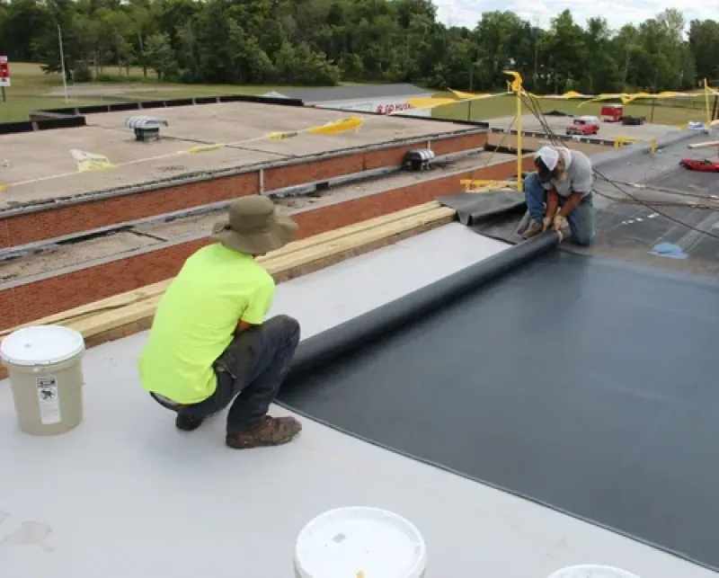 Workers applying black roofing membrane on a flat roof under construction.