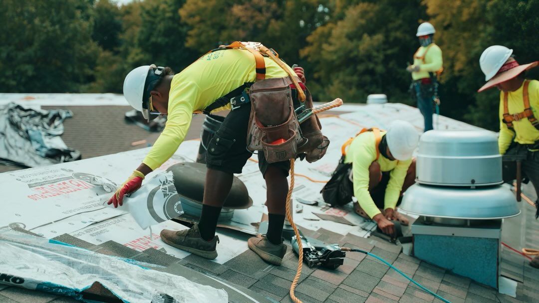Workers on a rooftop repairing damaged shingles near a white vent pipe and tools