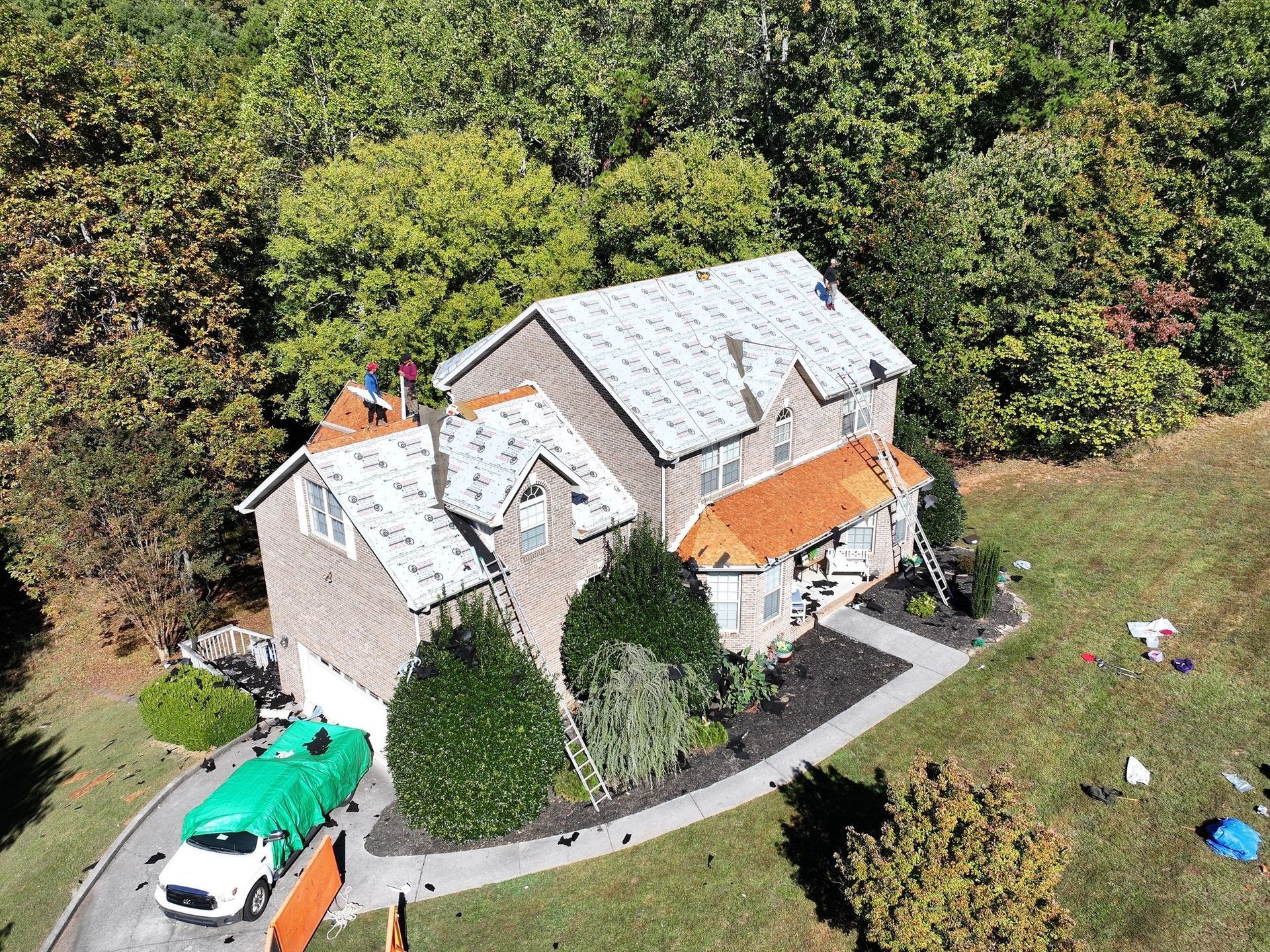Aerial view of a house with a white roof, orange awnings, and a driveway beside trees and lawn.