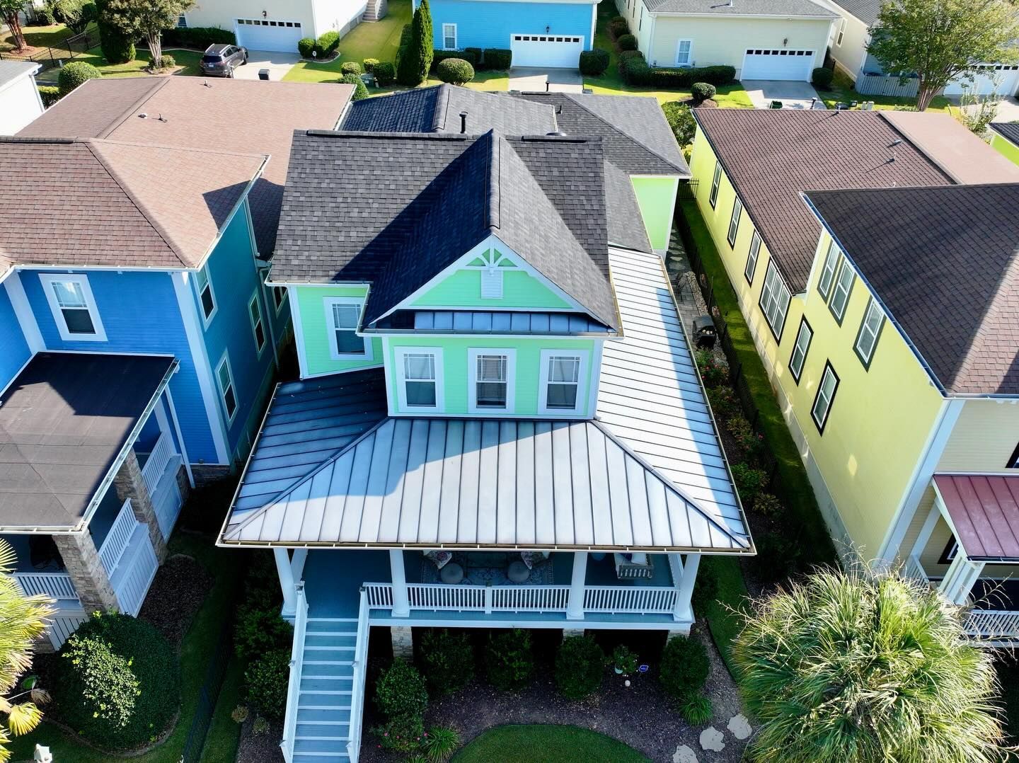 Aerial view of colorful suburban houses, centered on a blue home with a white porch and gray roof.