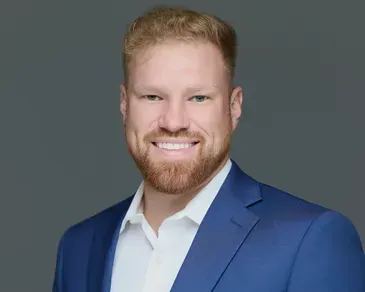 Smiling man in a blue suit jacket and white shirt against a gray background