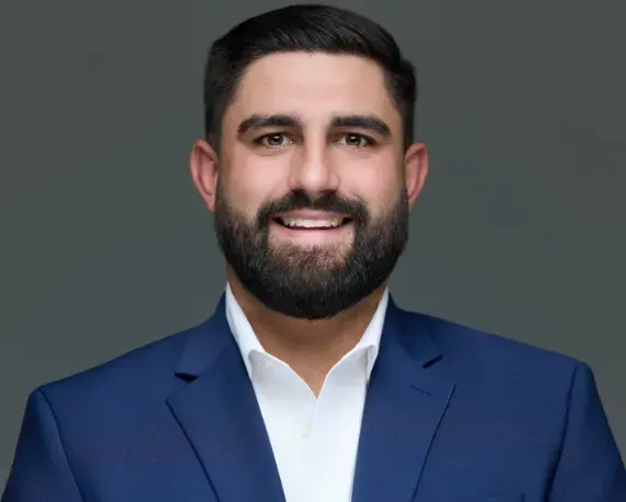 Smiling man in a navy suit and white shirt against a gray background
