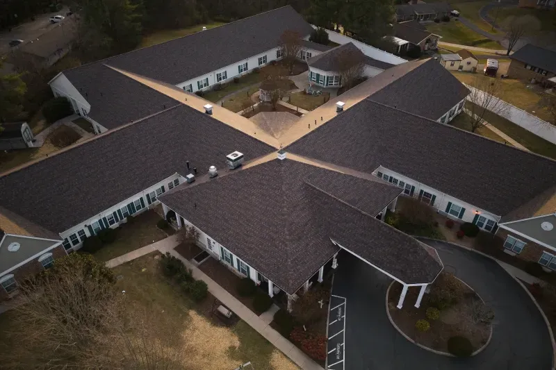 Aerial view of a beige building complex with dark roofs and a central courtyard.