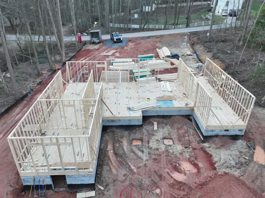 Construction site with wooden house framing on red dirt, viewed from above