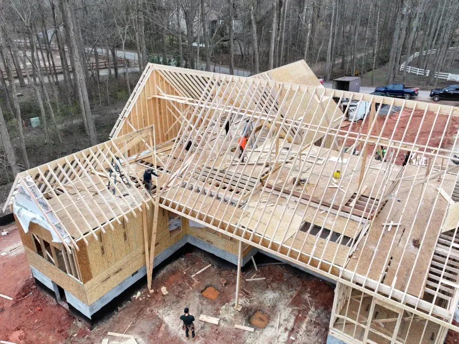 Workers framing the roof of a house under construction with exposed wooden beams.