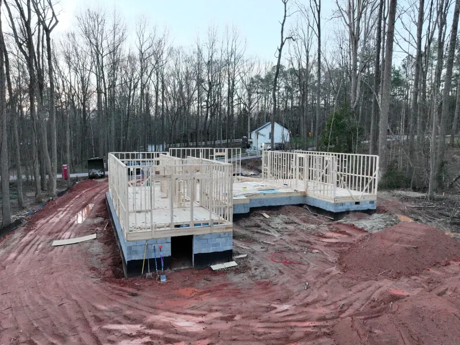 Partially built wooden house foundation on red muddy ground in a bare wooded area