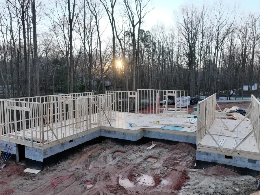 Partially built house foundation with wooden framing at sunset in a wooded lot