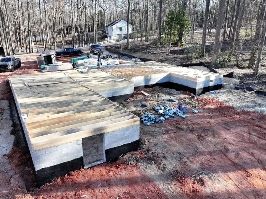 Wooden deck foundation under construction beside a wooded yard, with stacked materials and blue foam insulation.