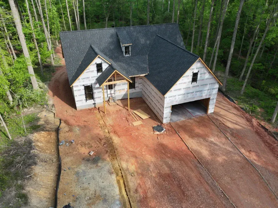 Aerial view of a house under construction on a cleared lot beside a forest
