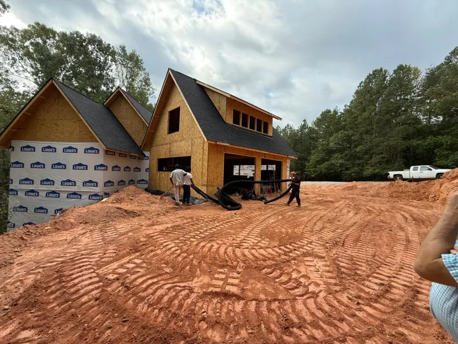 New houses under construction on a red dirt lot, with workers and building materials visible