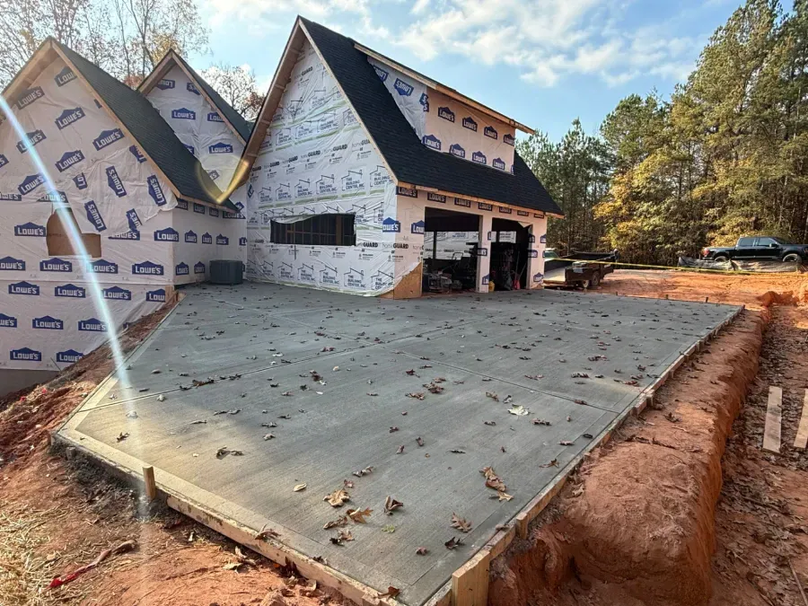 Partially built house wrapped in house wrap, with a large concrete slab and dirt lot in front