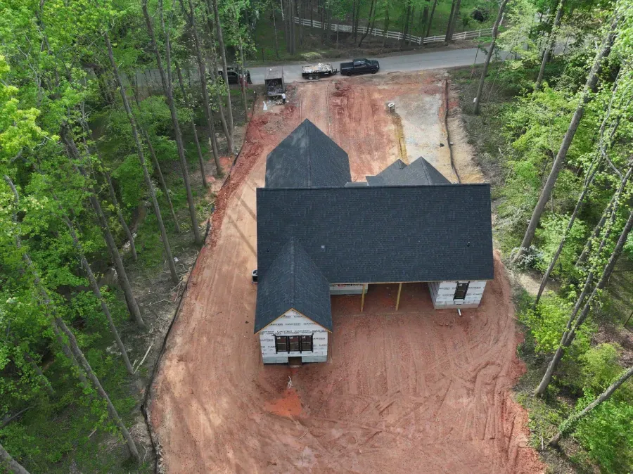 Aerial view of a black-roofed house on a red dirt lot surrounded by trees