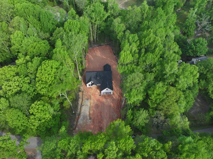 Aerial view of a house with a red driveway surrounded by dense green trees