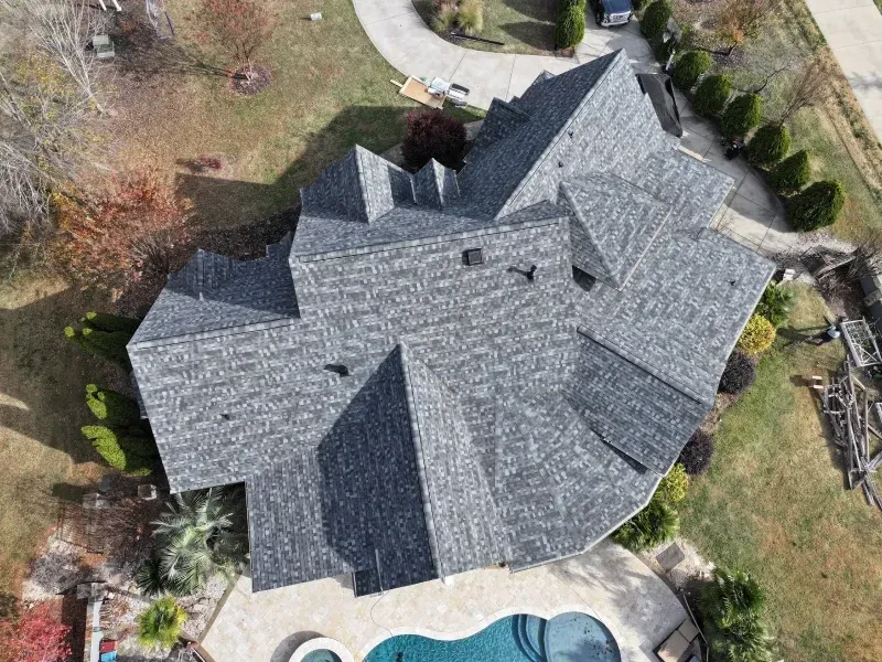 Aerial view of a gray-shingled house with a curved driveway and surrounding trees