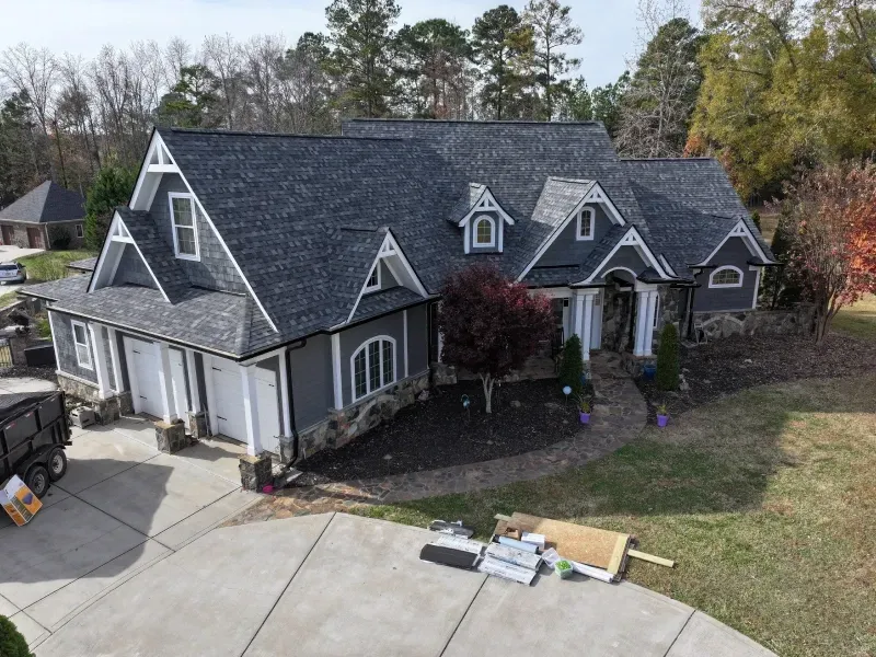 A large gray two-story house with dormer windows, a driveway, and scattered items on the front lawn.