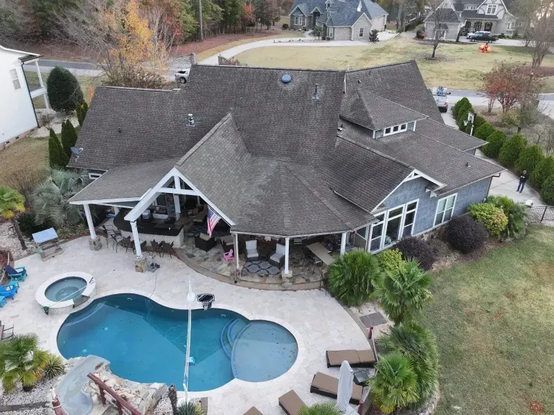 Aerial view of a house with a backyard pool, patio seating, and landscaped yard.